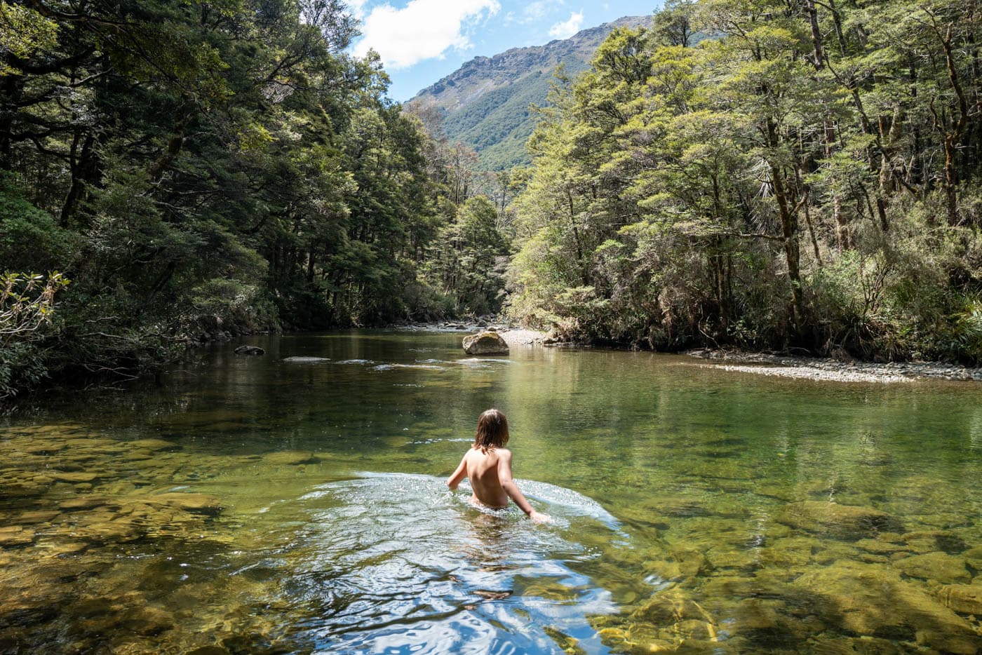 Clear river pool surrounded by rocks and native bush, inviting for swimming in New Zealand